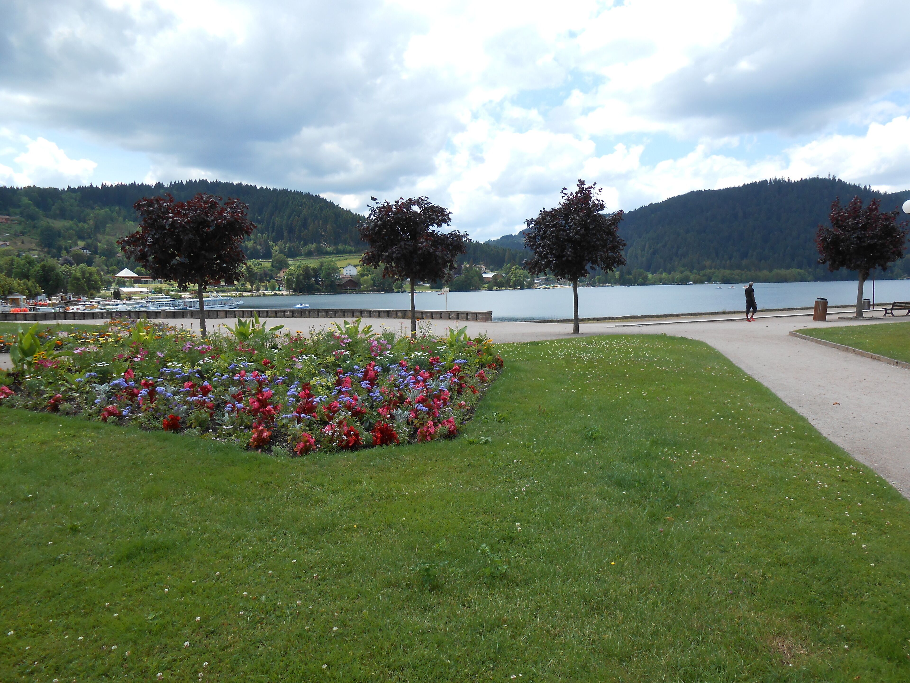 Ein Park mit Blumenbeeten, einem Fußweg und einem See, dessen Hintergrund von Bergen gebildet wird.