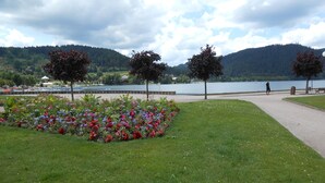A park with a flower bed, a walking path, and a lake with mountains in the background.