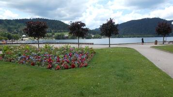 Ein Park mit Blumenbeeten, einem Fußweg und einem See, dessen Hintergrund von Bergen gebildet wird.