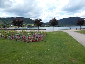 Un parque con un jardín de flores, un sendero para caminar y un lago con montañas al fondo.