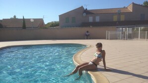 Une piscine à l’eau claire, une terrasse carrelée et, au fond, un bâtiment avec un toit recouvert de tuiles.