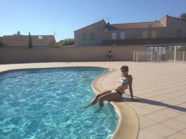 A swimming pool with clear water, a tiled deck, and a building with a tiled roof in the background.