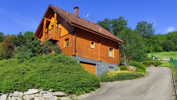 Una casa a due piani in legno, con tetto spiovente, fondamenta in pietra e vialetto lastricato.
