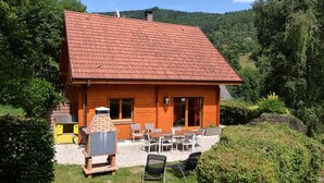 Una baita in legno con tetto in tegole rosse, un patio con mobili da esterno e un camino.