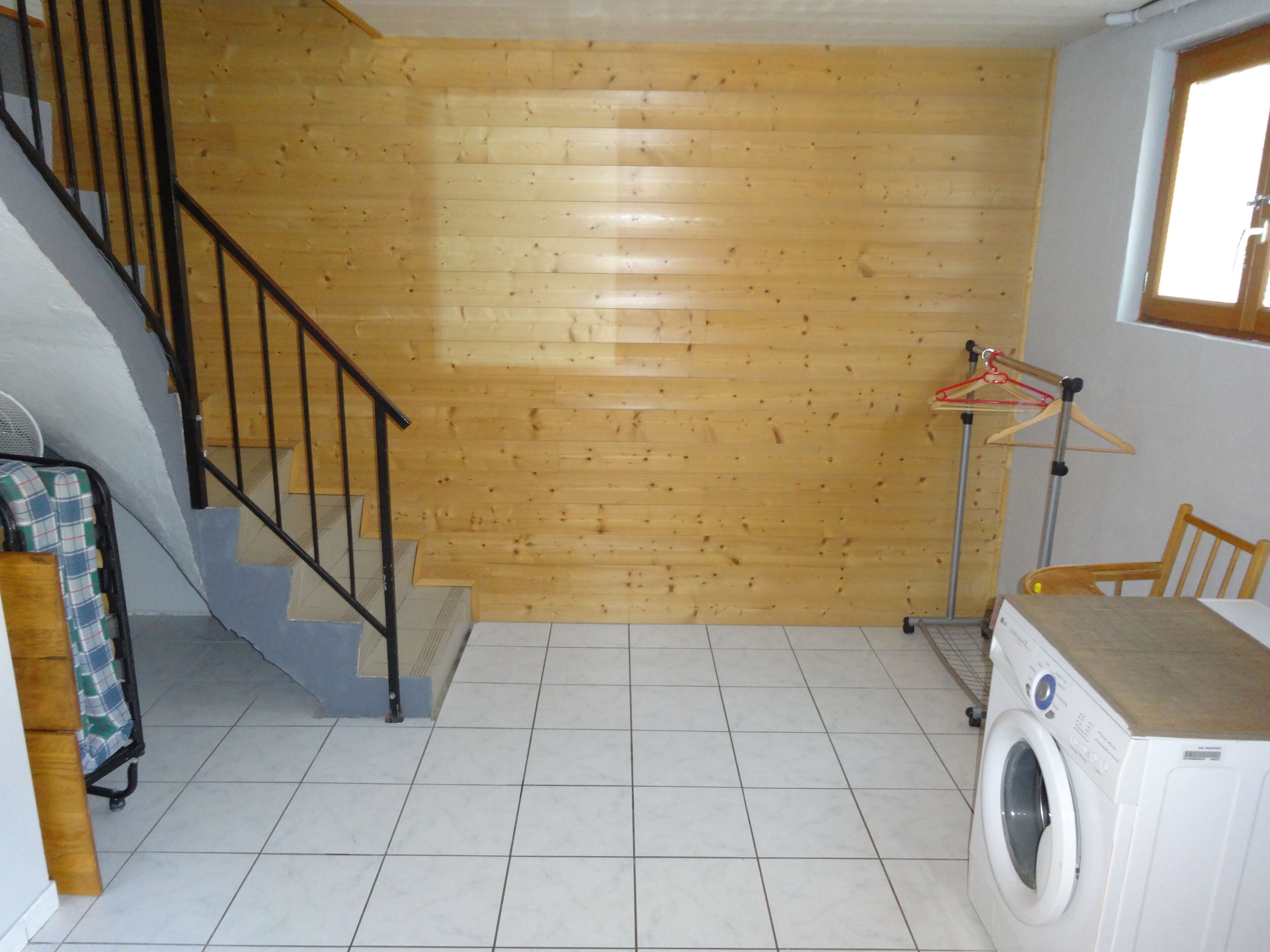 Ein Waschraum mit Waschmaschine, Wäscheständer, Stuhl und einer Treppe zu einem anderen Raum.