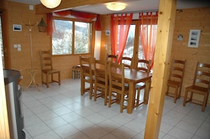 Un interior de madera con una mesa de comedor y sillas, ventanas grandes con cortinas, y piso de madera.