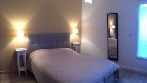 Un dormitorio con una cama, dos mesitas de noche, un tocador, un espejo y una ventana.
