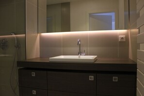 Ein modernes Badezimmer mit einem rechteckigen Waschbecken, einem Spiegel darüber und einer Dusche links.