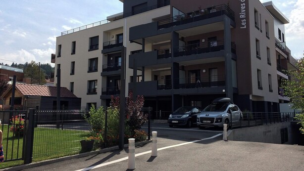 Un edificio residencial de varios pisos con balcones, zona de estacionamiento y entrada protegida por un portón.