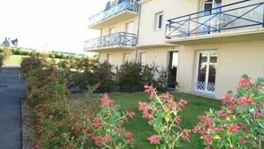 Ein mehrgeschossiges Wohngebäude mit Balkonen, einer gepflasterten Auffahrt und einem gepflegten Garten mit blühenden Pflanzen.