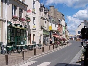 Une rue bordée d’immeubles, avec des terrasses et une enseigne indiquant « La Petite Café ».