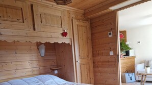 Una habitación de madera con una cama, una lámpara colgante y una puerta que da a otra habitación.