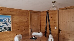 Un comedor de madera con una mesa redonda, sillas blancas de aspecto mullido y un cuadro de montañas en la pared.