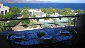 Un balcon avec une table dressée pour le dîner, offrant une vue sur un paysage côtier avec des bâtiments et des arbres.