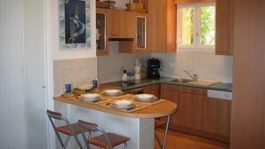 Une cuisine compacte avec des meubles en bois, un îlot central doté de tabourets, une machine à café et une fenêtre laissant entrer la lumière naturelle.
