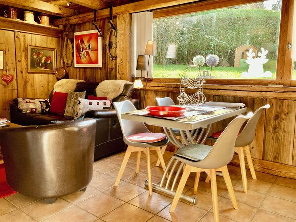 A cozy cabin interior with a dining area, wooden walls, and a view of a garden. - GARDEN GROUND IN CHALET WITH WIFI CLASS 3 STARS (Chamonix-Mont-Blanc)