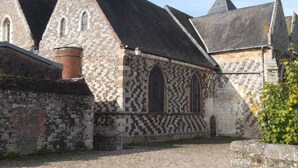 Un bâtiment historique doté d’une façade en pierre, de fenêtres en arc de cercle et d’un porche carrelé.