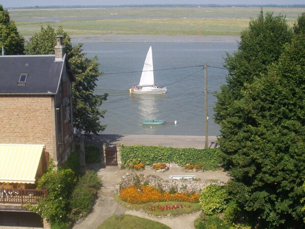 Un velero en aguas tranquilas, rodeado de follaje y un edificio con fachada de ladrillo.