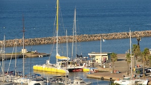 Un port de plaisance avec des bateaux amarrés, une digue rocheuse et un petit bâtiment sur lequel on peut voir une enseigne.