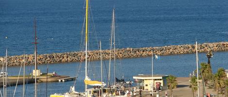 Un port de plaisance avec des bateaux amarrés, une digue rocheuse et un petit bâtiment sur lequel on peut voir une enseigne.