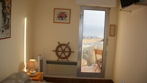 Une chambre à coucher avec un lit, une table de chevet avec une lampe, un gouvernail de bateau fixé au mur, un tableau encadré et un balcon offrant une vue sur la ville.