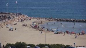 Une plage avec des gens, des parasols et une côte rocheuse.