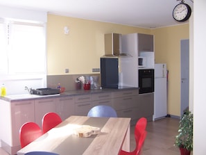 A compact kitchen with a dining area, featuring a wooden table, red chairs, and basic appliances. - Bed and breakfast (Ban-De-Laveline)