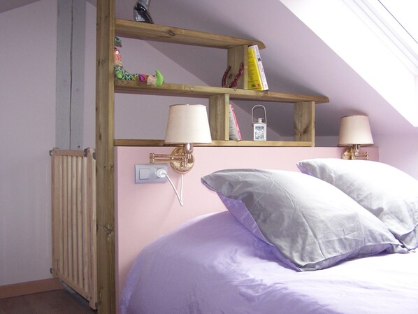 A bedroom with a sloped ceiling, a wooden shelf with books and a lamp, a radiator, and two bedside lamps. - Bed and breakfast (Ban-De-Laveline)
