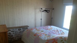 A bedroom with a bed, a wooden nightstand, a stone wall, and a window. - 2 * house for 6 people direct access to the sea (Bouin)