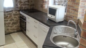 A kitchen with stone walls, a black countertop, white cabinets, a built-in microwave, and a stainless steel sink. - 2 * house for 6 people direct access to the sea (Bouin)