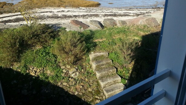 A coastal view with a rocky shoreline, a grassy area, and a distant cityscape. - 2 * house for 6 people direct access to the sea (Bouin)