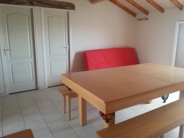 A room with a wooden table, a red chair, and a wooden bench. There are white doors and a tiled floor. - 2 * house for 6 people direct access to the sea (Bouin)