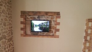 A room with a stone wall, a television mounted on a brick wall, a wooden bench, and a black leather sofa. - 2 * house for 6 people direct access to the sea (Bouin)