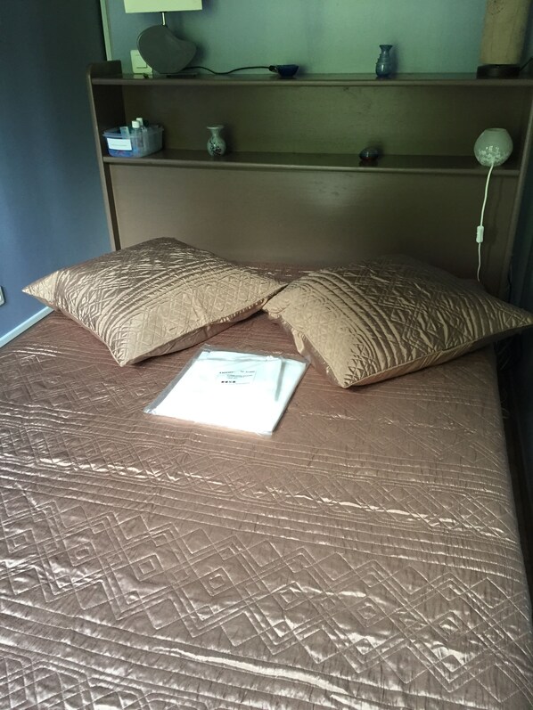 A bed with a patterned bedspread, two pillows, and a white envelope on the bed. - Apartment in luxury residence downtown (Cauterets)
