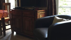 A living room with a flat-screen TV on a wooden cabinet, a dark leather sofa, and a wooden chair with a plaid tablecloth. - Apartment in luxury residence downtown (Cauterets)