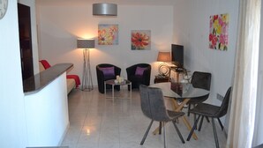 A modern living room with a glass dining table, two armchairs, a sofa, and a floor lamp.