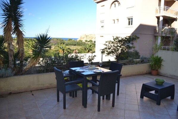 Patio esterno con tavolo e sedie, uno sgabello e piante in vaso.