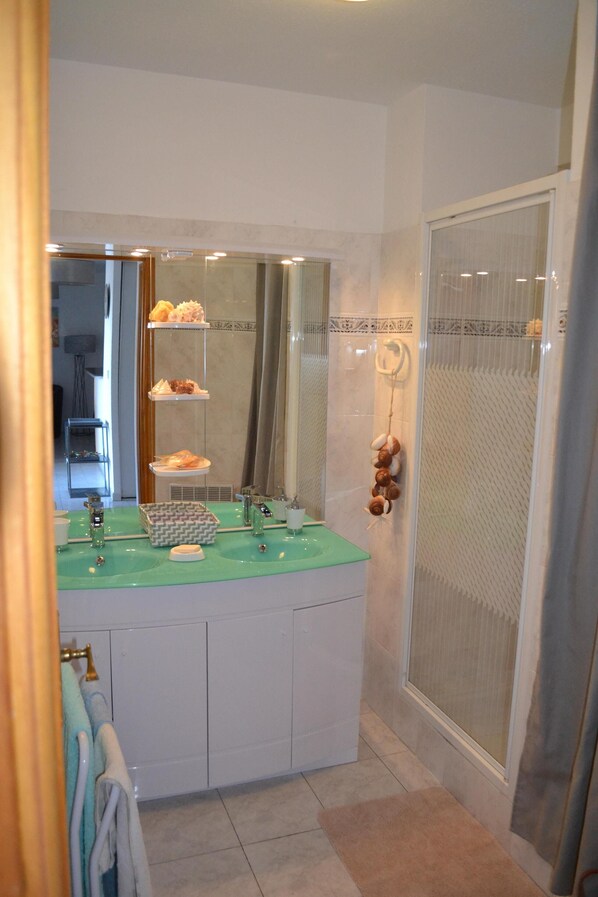 Une salle de bain avec un meuble-lavabo blanc, un plan de toilette vert, un miroir, une douche avec une porte en verre et un porte-serviettes.