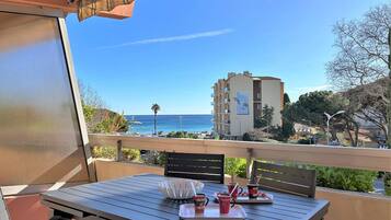 Un balcon avec une table et des chaises, donnant sur une plage et un bâtiment d’hôtel.
