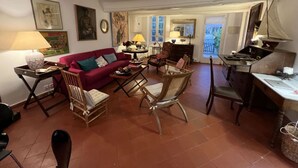Ein gemütliches Wohnzimmer mit einem roten Sofa, Holzstühlen, einem kleinen Tisch und einem Schreibtisch.