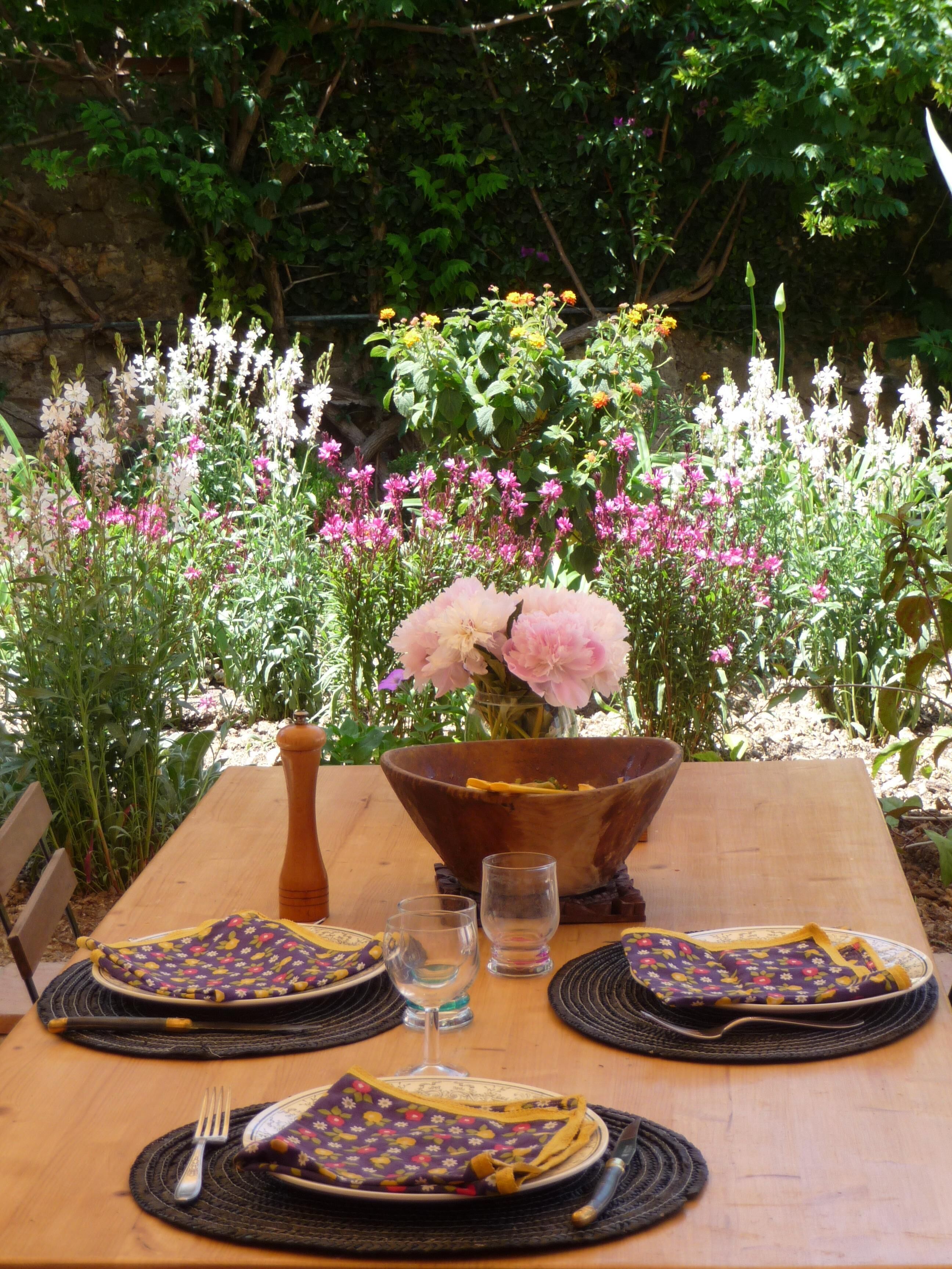 Une table de jardin, dressée pour un repas en plein air, avec des assiettes, des couverts et un vase rempli de fleurs.