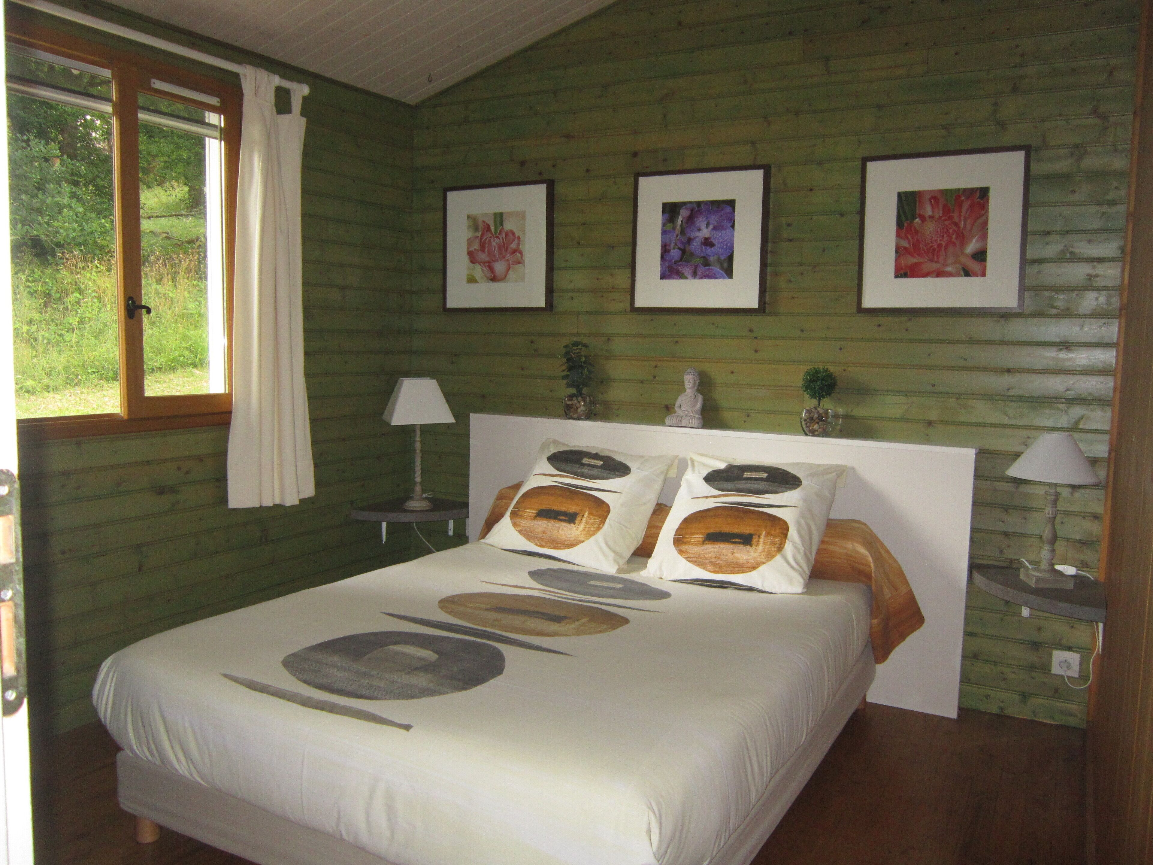 A bedroom with a bed, a window, a nightstand, a lamp, and three framed pictures on the wall.