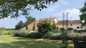 A garden with a lawn, a potted plant, and a house with a red roof in the background. - CHARMING FAMILY HOME (Baigts)