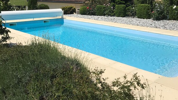 A swimming pool with a tiled deck, surrounded by greenery and a house with a tiled roof. - CHARMING FAMILY HOME (Baigts)