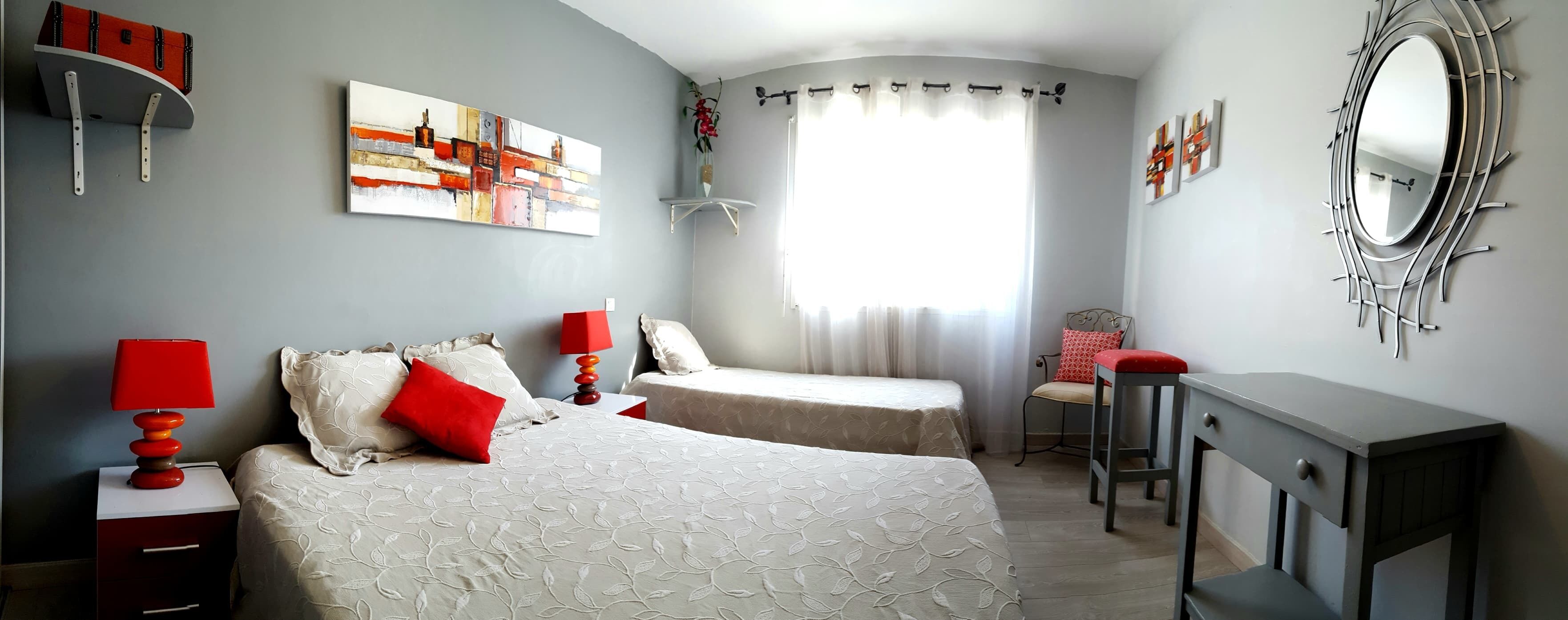 A bedroom with two beds, a desk, a chair, a mirror, and artwork on the walls.