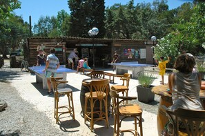 Un espace extérieur aménagé avec des tables et des chaises, une table de ping-pong et une structure en bois portant une enseigne.
