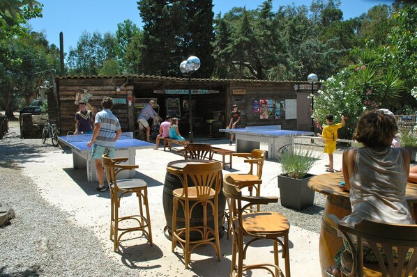 An outdoor seating area with tables and chairs, a ping pong table, and a wooden structure with a sign.