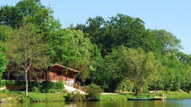 Una cabaña de madera junto a un lago, rodeada de árboles densos.