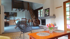 Amplia sala de estar con una escalera de madera, una mesa de comedor con un jarrón de flores y una chimenea.