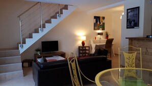 A modern living room with a staircase, a flat-screen TV, a sofa, a glass table, and a dining area with chairs. - TOP-OF-THE-RANGE DUPLEX 95 m2 GARDEN GROUND TO 1.8 KM SKI STATION (Bellefontaine)